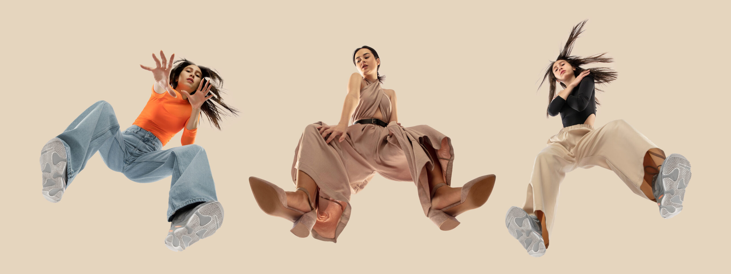 Young stylish women in modern street style outfit isolated on brown background, view from the bottom. Fashionable models, musicians, rappers performing.